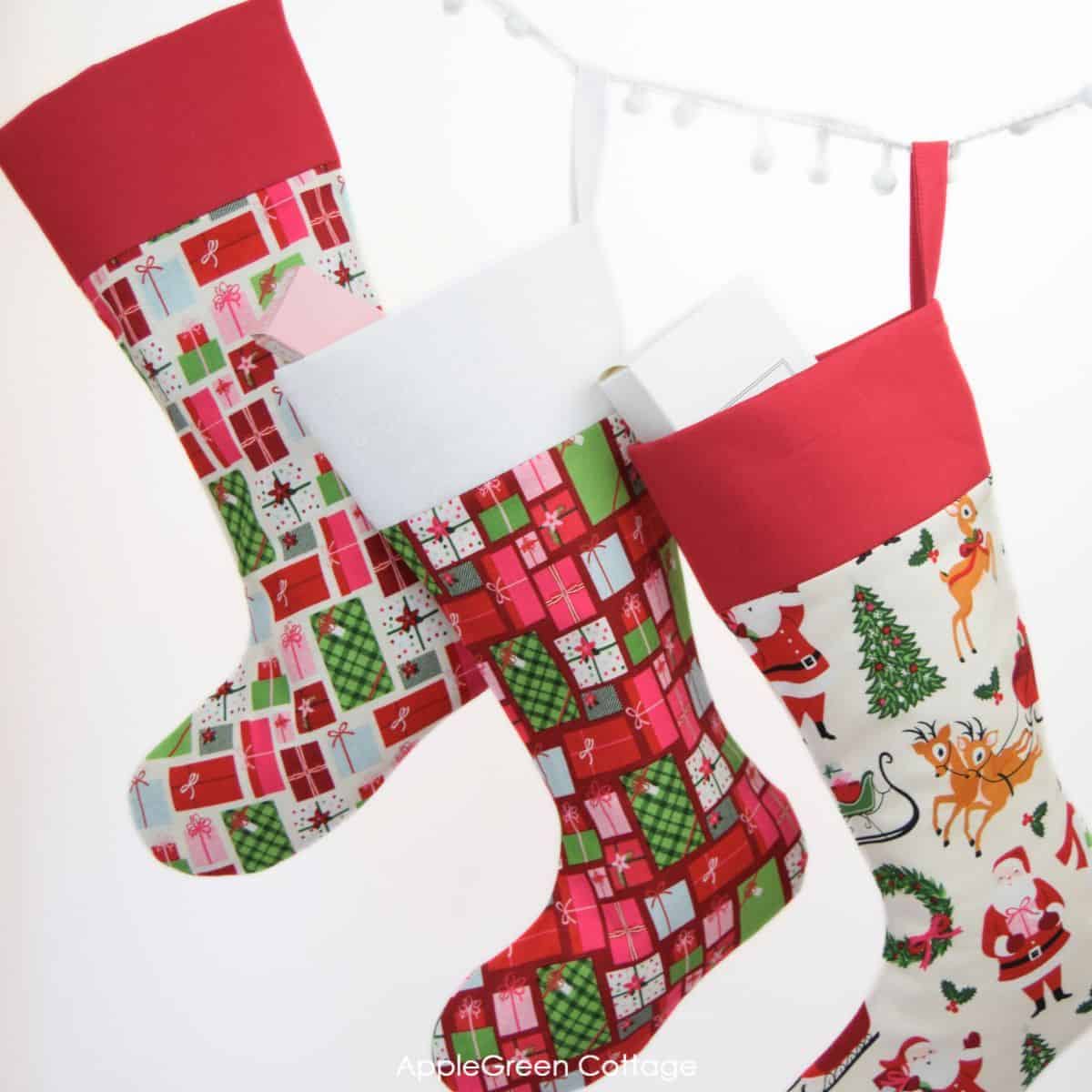 three finished christmas stockings in christmas cotton prints hanging on a pompom rope sewn with a free Christmas stocking pattern